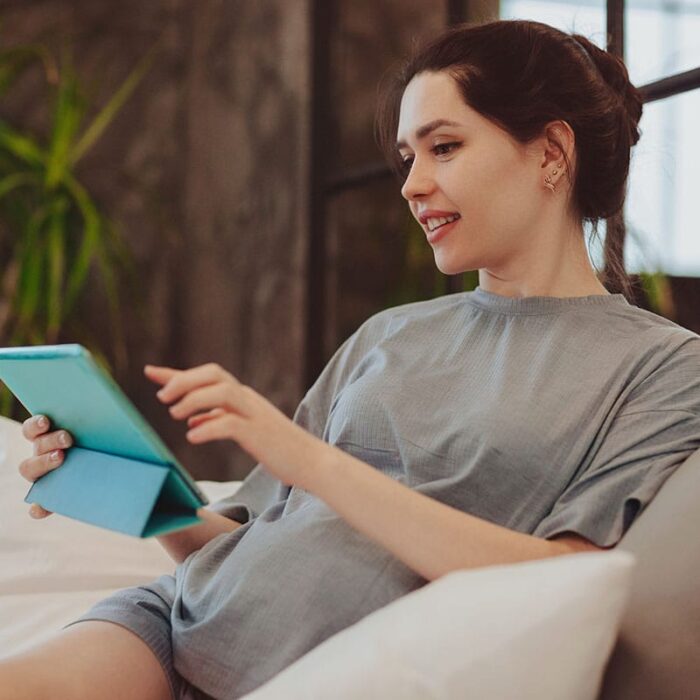 young woman seated comfortably and reviewing the 5 benefits of telehealth on her wireless tablet