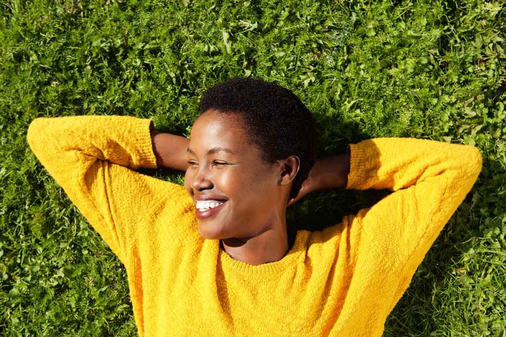 young woman lying on the grass on a sunny day and smiling after adopting healthy coping mechanisms