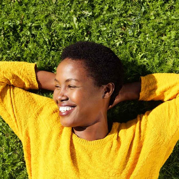 young woman lying on the grass on a sunny day and smiling after adopting healthy coping mechanisms