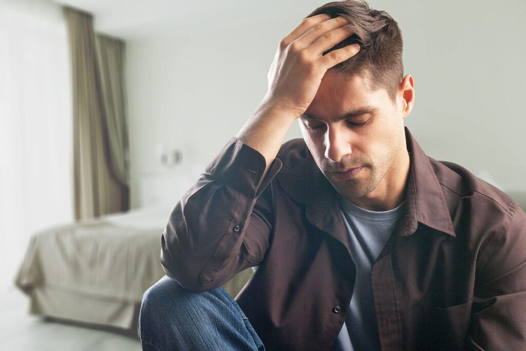 troubled young man seated on couch with his head in his hands and struggling with common types of depression