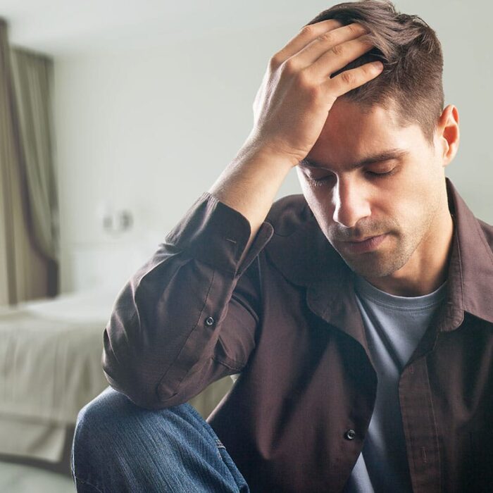 troubled young man seated on couch with his head in his hands and struggling with common types of depression