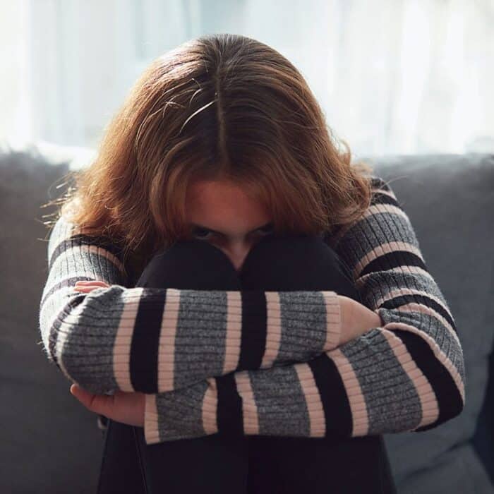 troubled young woman sitting on couch with knees pulled up to chest and arms wrapped around herself attempting to understand what is high functioning anxiety