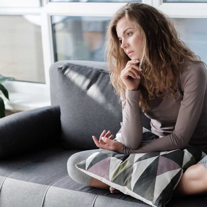 woman sitting on couch and staring blankly into space ass she struggles with living with anxiety