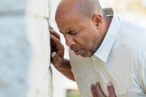 middle aged man hunched over in pain and clutching chest while leaning against the wall and recognizing the signs of an anxiety attack