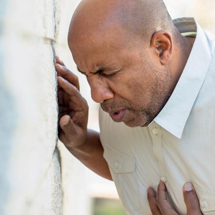 middle aged man hunched over in pain and clutching chest while leaning against the wall and recognizing the signs of an anxiety attack