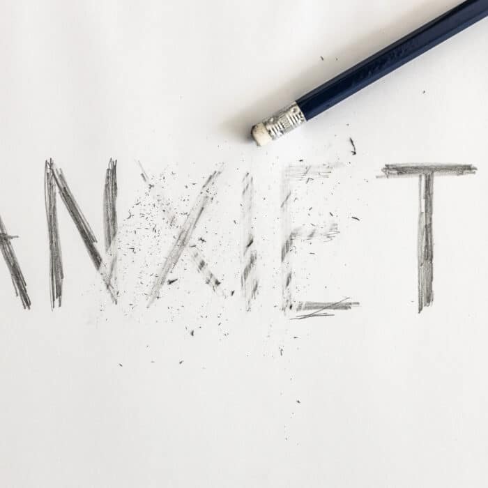 Erasing anxiety. Anxiety written on white paper with a pencil, partially erased with an eraser. Symbolic for overcoming anxiety or treating anxiety.